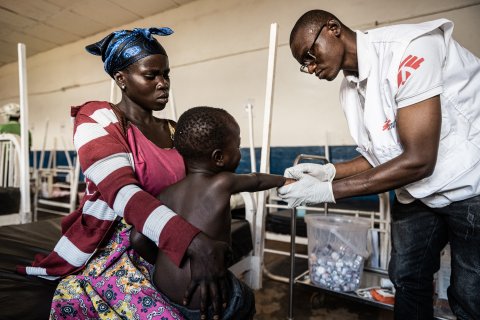 Doktor undersöker barn som sitter i mammans knä.
