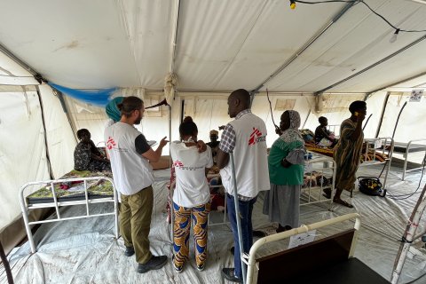 Läkare Utan Gränsers anställda står i ett stort uppbyggt tält med sjukvårdssängar och patienter runt om.