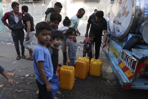 barn och vuxna köar för att hämta vatten vid en vattentank på en lastbil