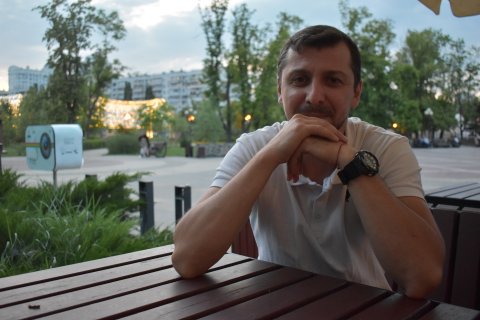 En man sitter utomhus vid ett bord och tittar in i kameran