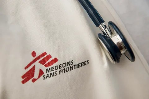 Närbild på Läkare Utan Gränsers logotyp tryckt på vitt tyg, till höger hänger ett stetoskop.