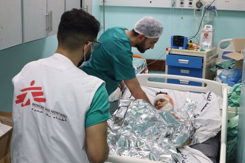 Medicinsk personal vid en sjukhussäng med en pojke med bandage runt huvudet