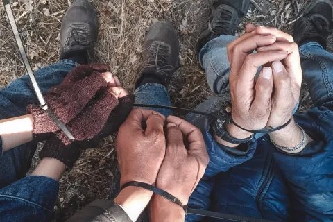 Närbild på flera par smutsiga händer som är ihopbundna med buntband