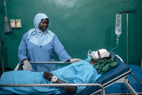 En sjuksköterska i operationskläder tar hand om en patient i en sjukhussäng