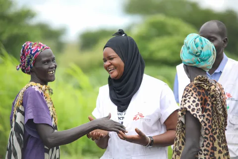 En kvinna i Läkare Utan Gränser väst och slöja skrattar tillsammans med två MSF volontärer.