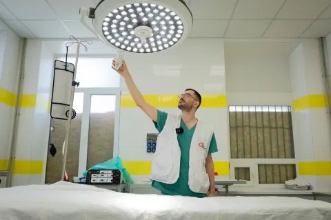 En sjukvårdsanställd med Läkare utan gränser-väst sträcker sig upp mot en lampa i en sjukhussal.
