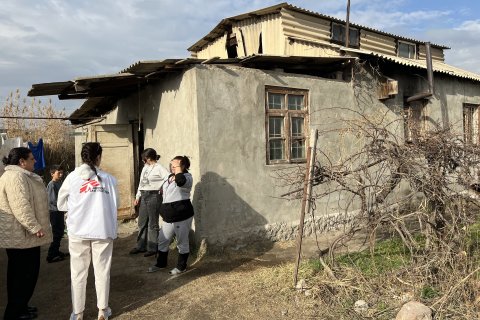 En kvinna med Läkare Utan Gränser-väst pratar med en grupp kvinnor utanför ett grått stenhus.
