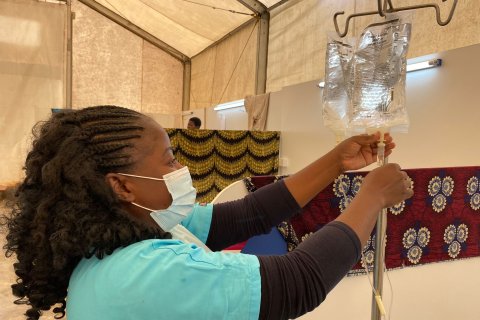 En kvinna i gröna sjukhuskläder och munskydd fixar till en påse dropp.