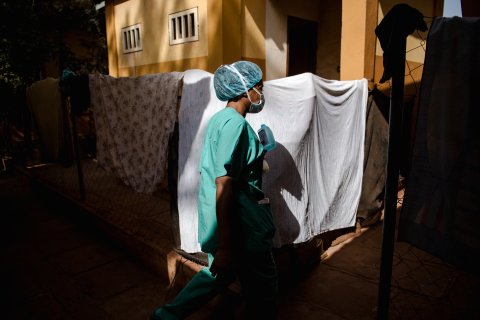 Kvinna iklädd sjukvårdskläder går framför lakan som hänger på tvättlina.