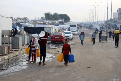 Flera människor bärandes på vattendunkar går längs en gata södra i Gaza.