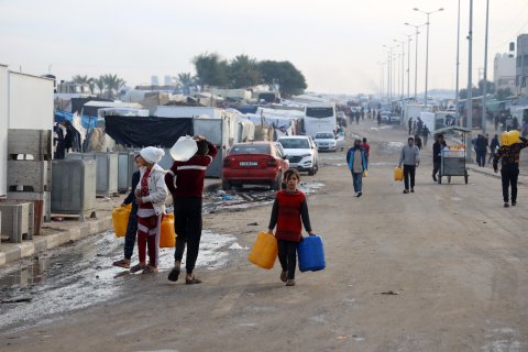 Flera människor bärandes på vattendunkar går längs en gata södra i Gaza.