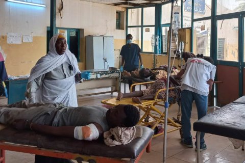 På sängar i ett rum ligger patienter omgivna av personal.