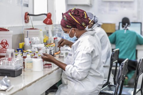 En kvinna i labbkläder och munskydd analyserar bakterieprov i ett laboratorium