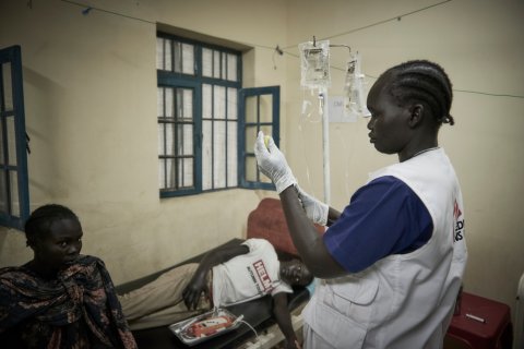 En kvinna med Läkare Utan Gränser-väst förbereder en spruta. På en brits bredvid ligger en person och en sitter bredvid.