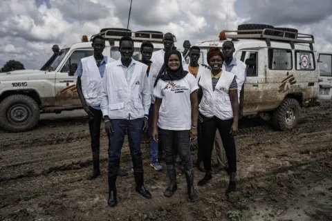 Personal från Läkare Utan Gränser tittar mot kameran framför en MSF-bil. 