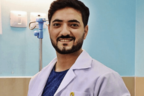 En man iklädd i en läkarrock från Läkare Utan Gränser ler och kollar in i kameran.