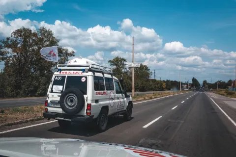 En ambulans med en flagga med Läkare Utan Gränsers logga på en rak asfalterad väg. 
