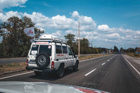 En ambulans med en flagga med Läkare Utan Gränsers logga på en rak asfalterad väg. 