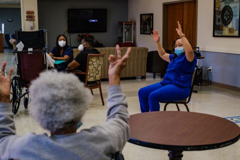 En sjukhusklädd kvinna sitter i en ring med äldre personer som sträcker upp armarna.
