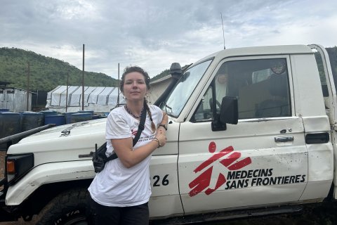 Kvinan står lutad mot bil, på bilen syns Läkare Utan Gränsers logotyp.