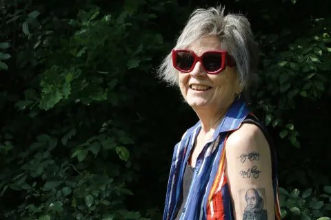 En person i stora solglasögon och många tatueringar på armen står utomhus