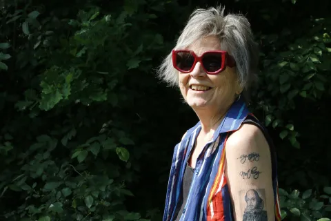 En person i stora solglasögon och många tatueringar på armen står utomhus