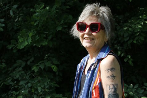 En person i stora solglasögon och många tatueringar på armen står utomhus