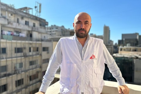 En man i Läkare Utan Gränser-väst står på en balkong med en stad i bakgrunden.