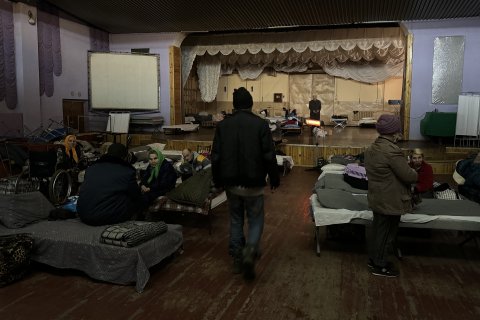 människor sitter en sal med en scen och rader av sängar