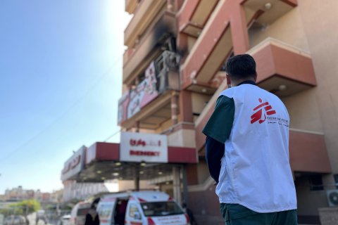 Man i Läkare Utan Gränser-väst utanför en byggnad med spår av angrepp