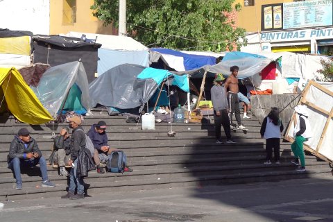 Tältläger i urban miljö. Två personer i Läkare Utan Gränser-västar pratar med en grupp migranter
