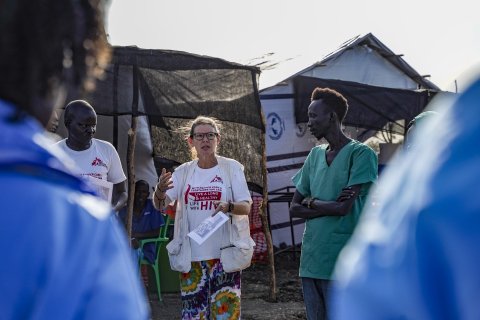 En kvinna i Läkare Utan Gränser-väst står utomhus med vårdklädda personer i en cirkel runt henne.