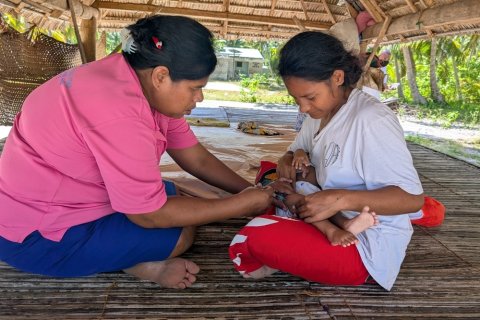 Två kvinnor sitter i skräddare mitt emot varandra. Den ena kvinnan har ett barn i knät som den andra kvinnan undersöker.