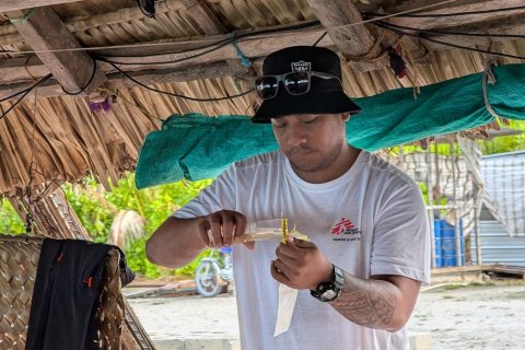 En man med Läkare Utan Gränser-tröja häller något från ett rör ner i en påse.