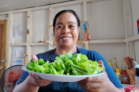 En leende kvinna håller fram ett fat med gröna grönsaker.