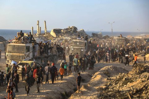 En lastbilskonvoj med förnödenheter möts av en stor mängd människor bland runier med havet som fond