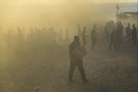 Folksamling i motljus. Man i förgrunden bär en kartong.