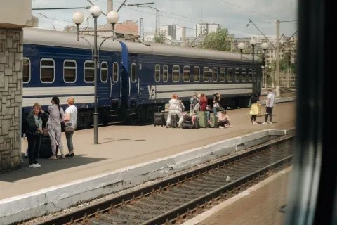 Tågräls och ett tåg med människor som väntar med väskor på perrongen.