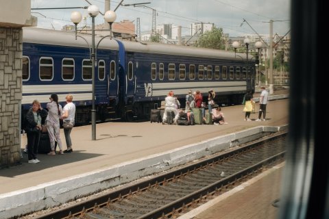 Tågräls och ett tåg med människor som väntar med väskor på perrongen.