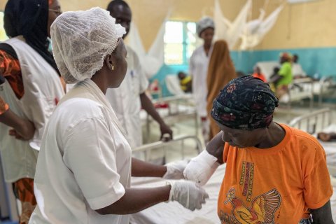 En kvinna i vita sjukhuskläder undersöker en kvinna med en bandagerad arm som slutar vid armbågen.