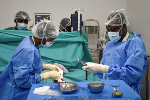 Två kirurger i heltäckande sjukhusdräkter, munskydd och handskar vid ett bord med sjukvårdsutrustning.