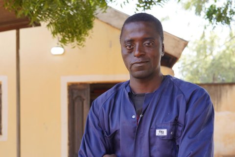 En man i blå overall med armarna i kors tittar in i kameran.