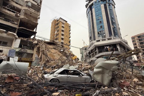 Ett stadsområde med kollapsade byggnader, där en krossad bil och stora rasmassor täcker gatan.