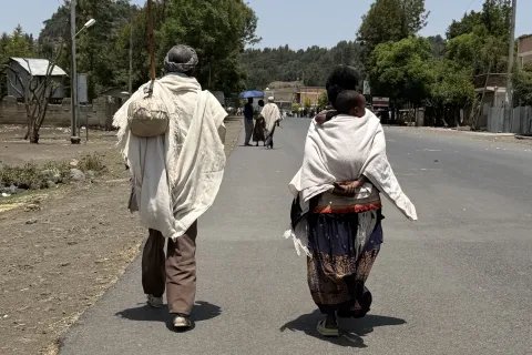 Två personer går längs en väg i Korem med träd och bebyggelse i bakgrunden.