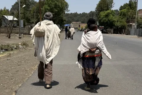 Två personer går längs en väg i Korem med träd och bebyggelse i bakgrunden.