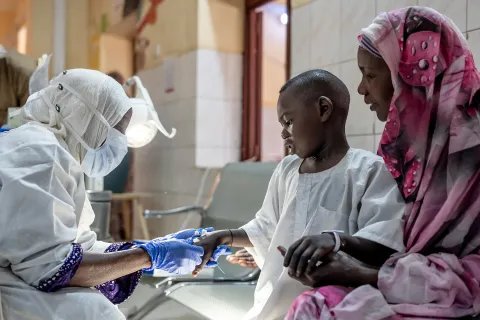 läkare från läkare utan gränser undersöker en pojkes hand medans han tröstas av sin mamma