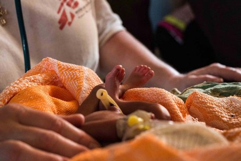 Små spädbarnsfötter sticker upp ut en orange filt med kroppen av en sjukvårdspersonal i bakgrunden