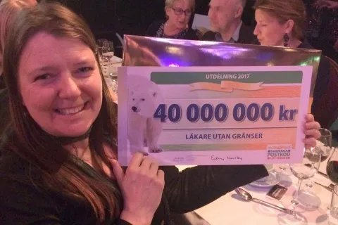 En kvinna håller upp en jättestor check från Postkodlotteriet