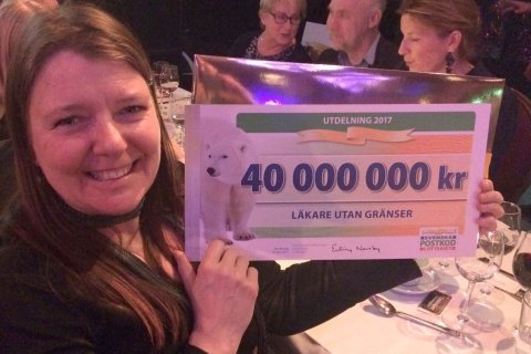 En kvinna håller upp en jättestor check från Postkodlotteriet