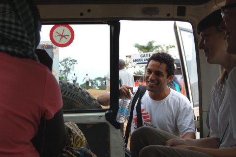 En läkare tittar in i en bil genom bakdörren och pratar med två firskförklarade patienter däri.